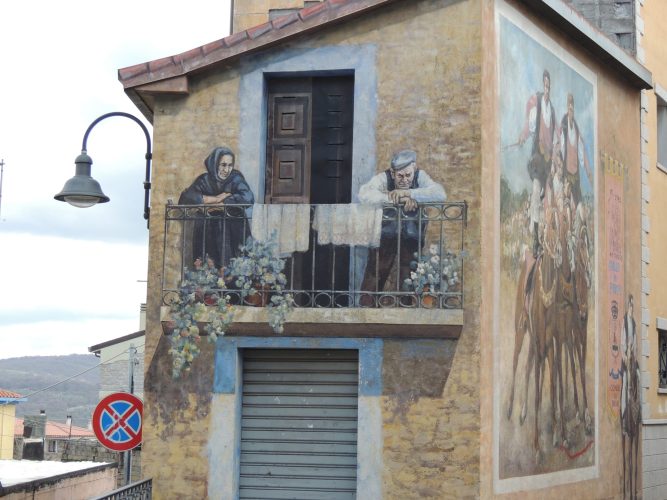 Realistische Wandmalereien in Fonni, Sardinien – ältere Personen auf Balkon und Reiterszene mit traditionellen Kostümen.